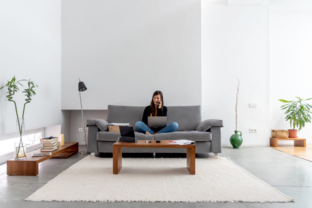 Young woman with laptop and phone telecommuting on the sofa at her home